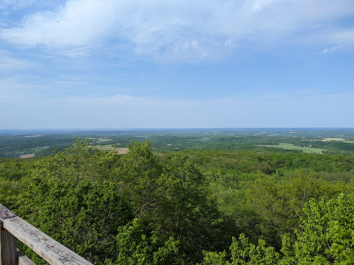 A panoramic view of lush green hills and valleys under a blue sky with scattered clouds.